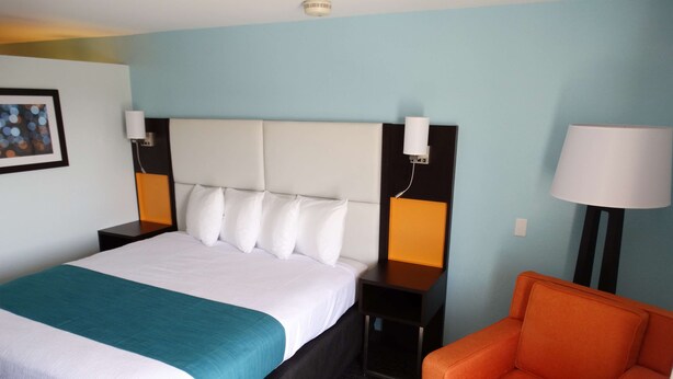 A hotel room with a large bed, two bedside tables, a nightstand, a chair, and a lamp. - Best Western Plus Orlando Lake Buena Vista South Inn & Suites (Kissimmee)