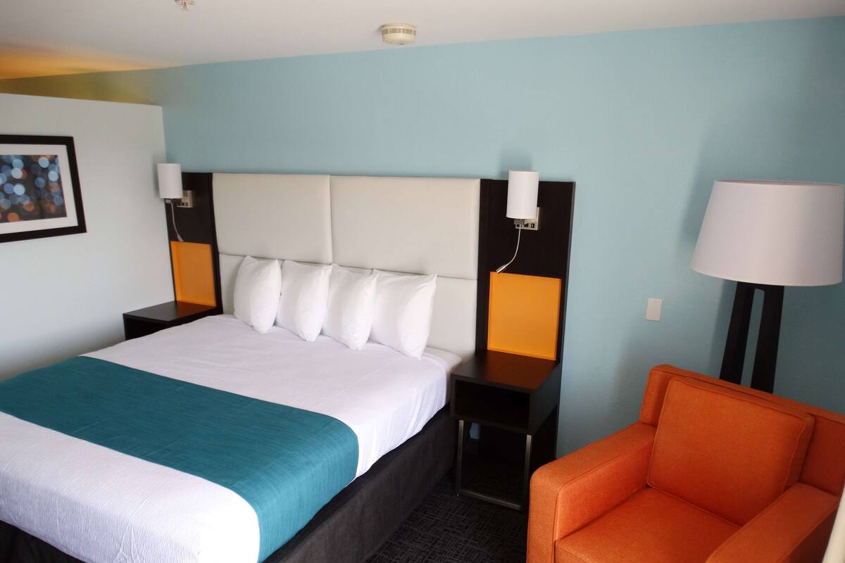 Ein Hotelzimmer mit einem großen Bett, zwei Nachttischen, einem Beistelltisch, einem Sessel und einer Lampe.