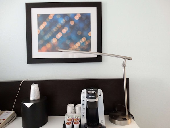 A hotel room with a framed abstract artwork, a Keurig coffee maker, a tissue dispenser, and a telephone.