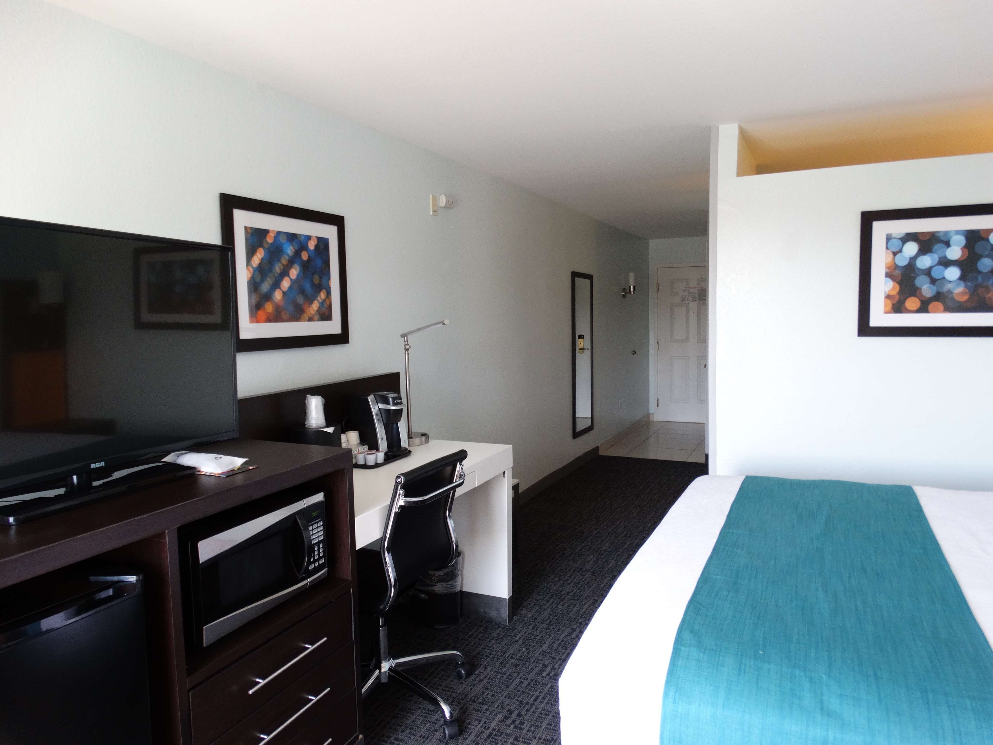 A hotel room with a bed, a desk with a computer, a coffee maker, and a TV.