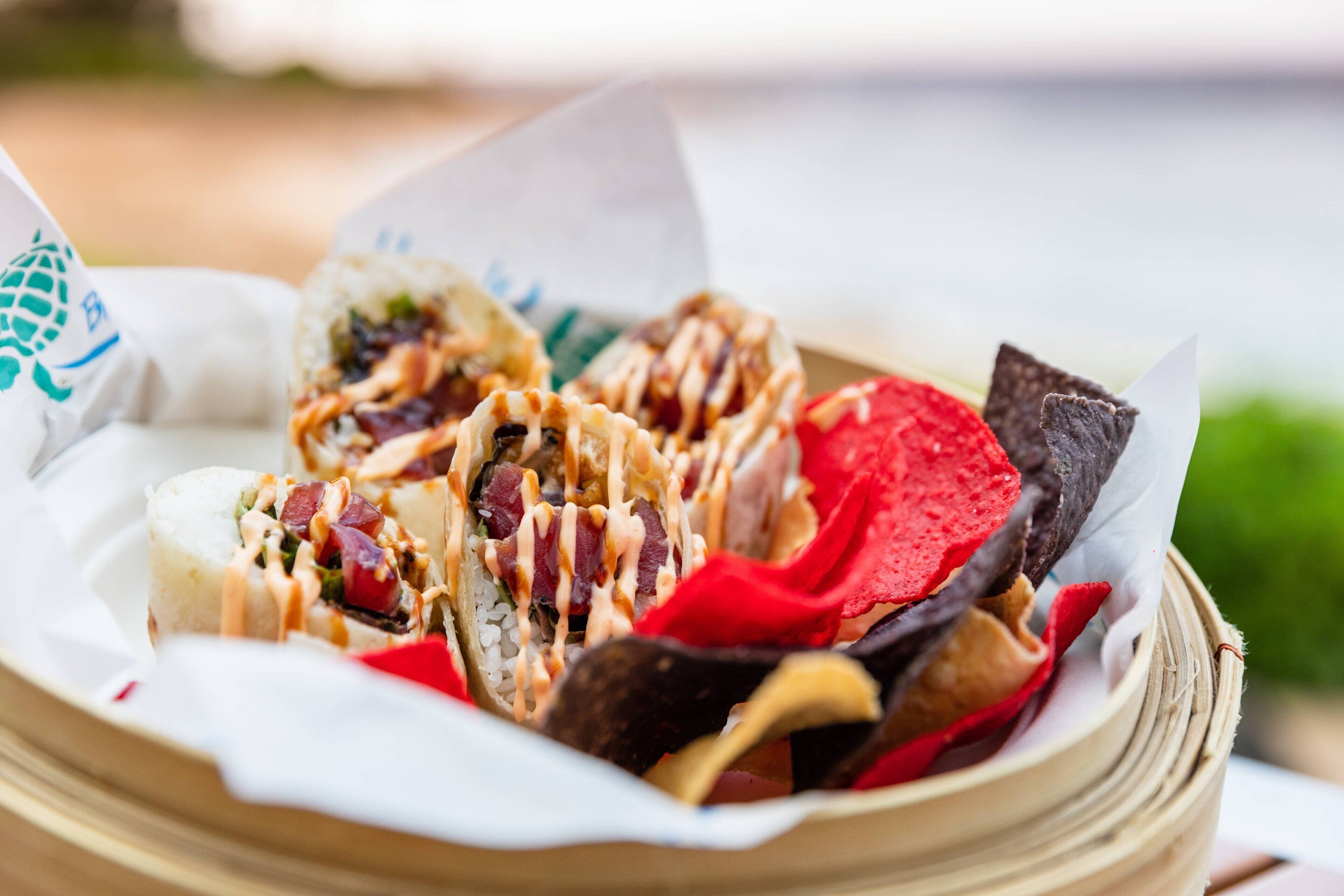 Una cesta con diversos alimentos, como sushi, cuencos de arroz y papas fritas.