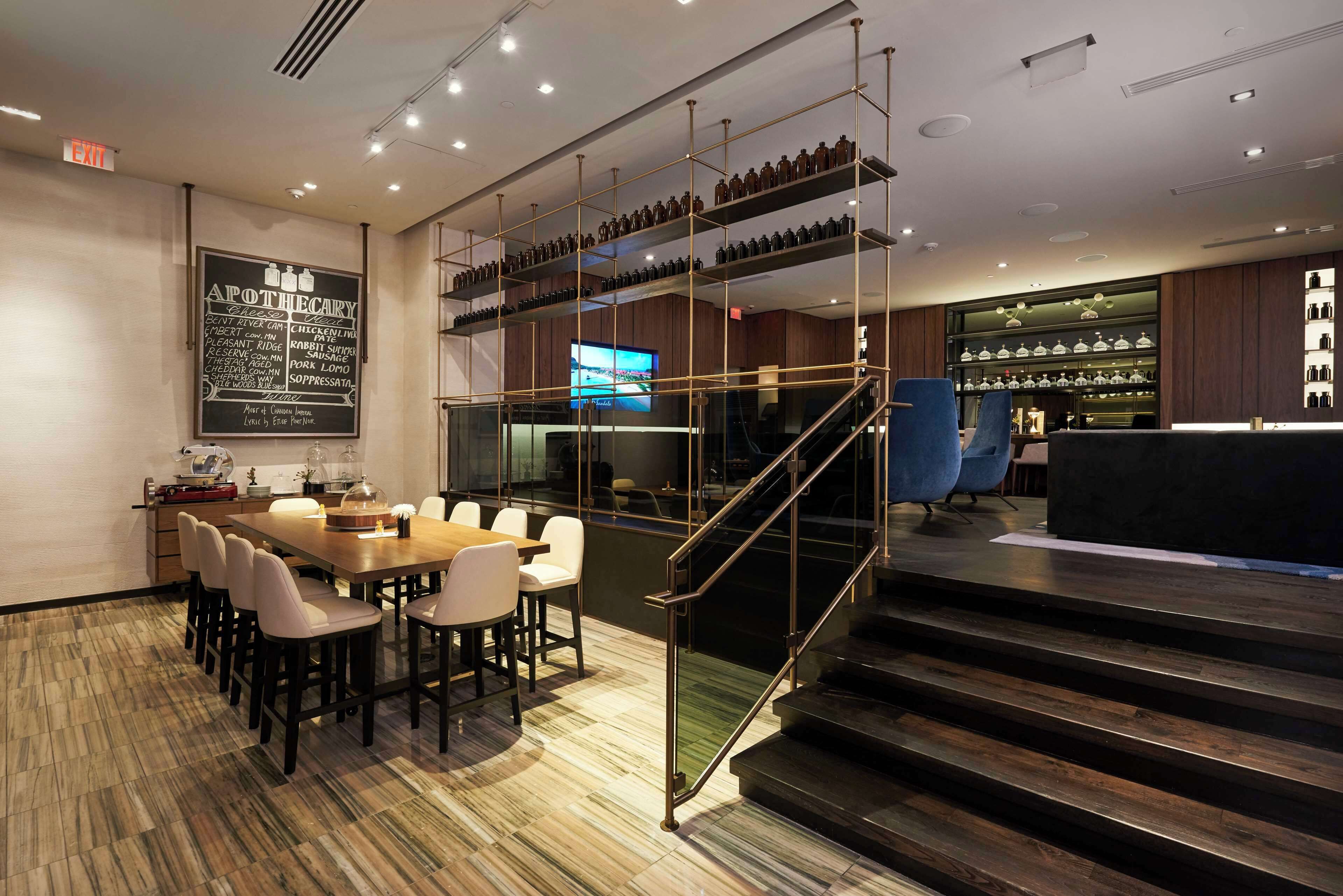 A modern restaurant with a wooden floor, a staircase, and a bar area with shelves of bottles.