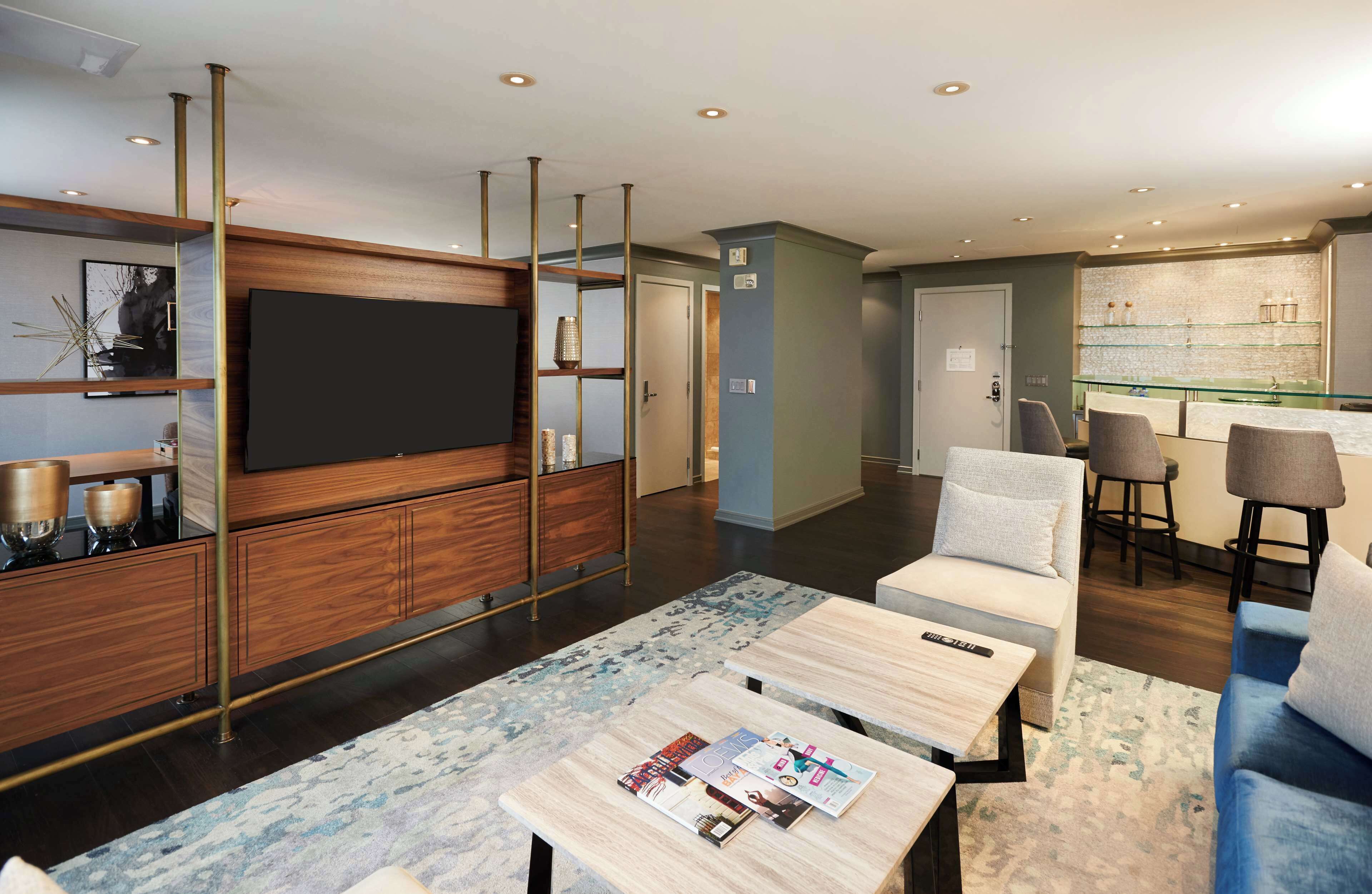 A modern hotel lobby with a flat-screen TV, wooden cabinets, a bar area, and seating.