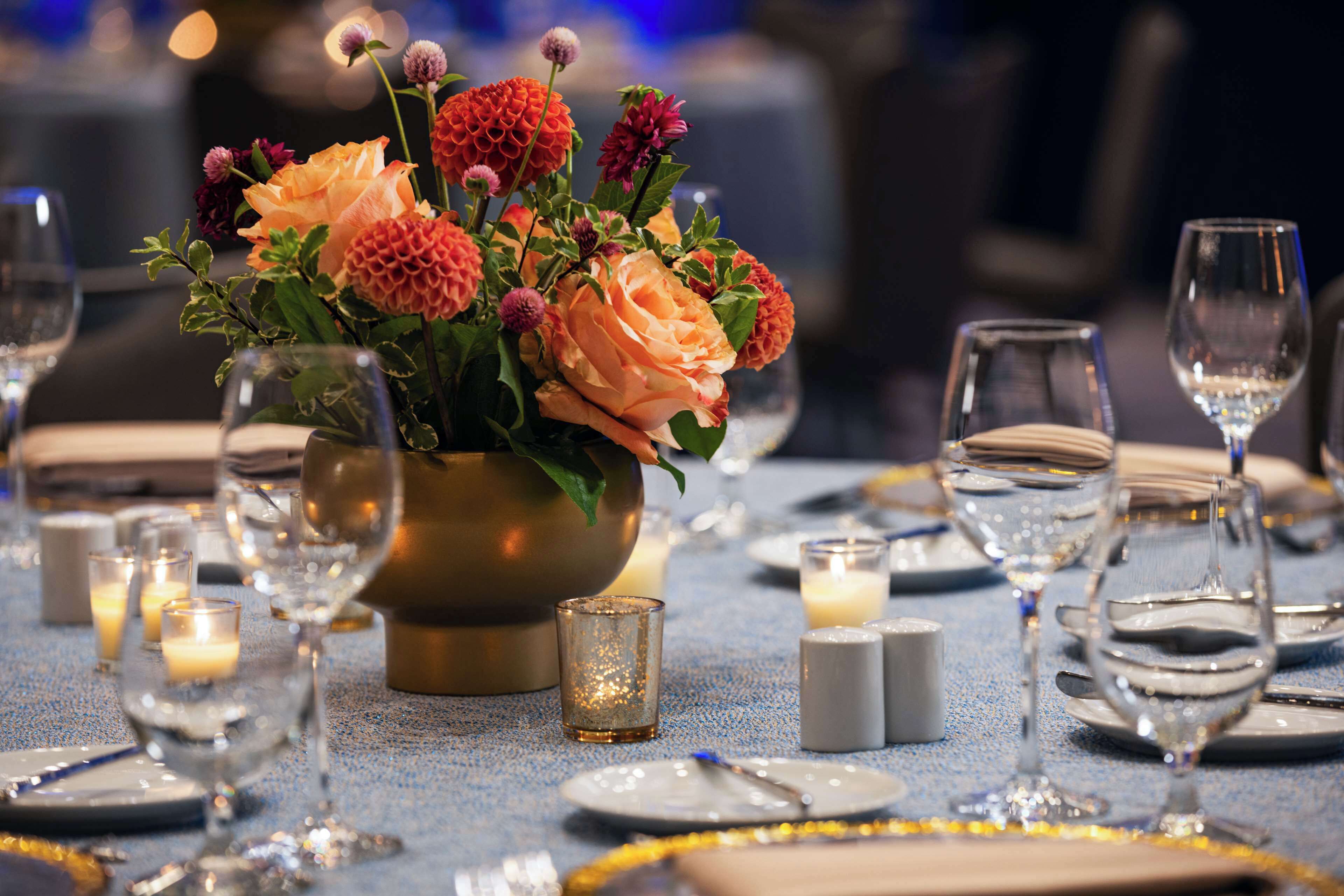 Une table dressée pour le dîner, agrémentée d’un centre de table composé de fleurs, de bougies et de verres transparents.