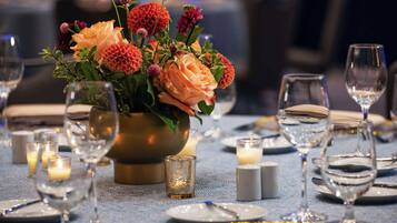 Une table dressée pour le dîner, agrémentée d’un centre de table composé de fleurs, de bougies et de verres transparents.