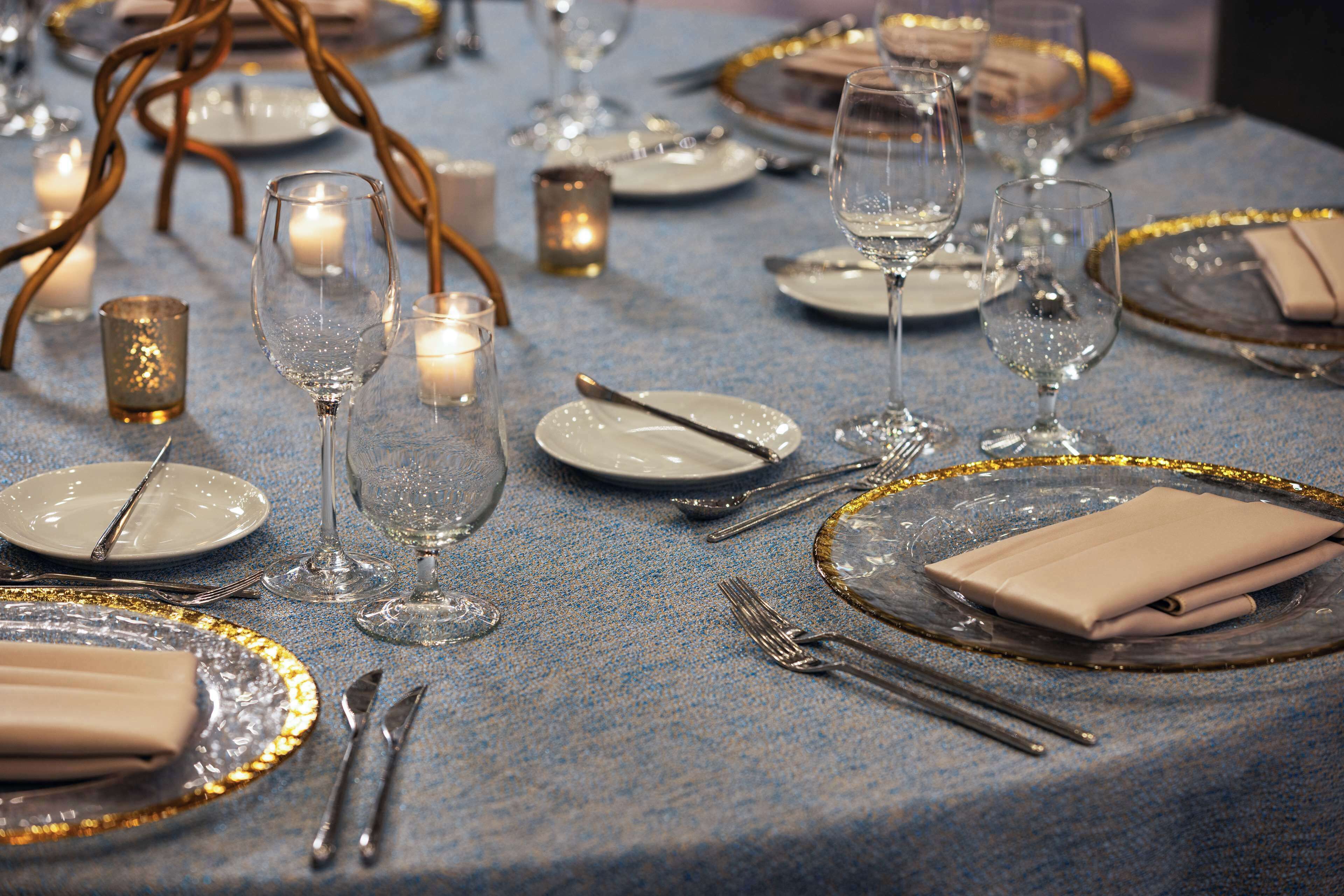 A table set with fine china, silverware, and wine glasses, with candles and a decorative centerpiece.