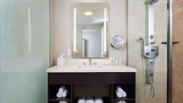 Une salle de bain moderne avec un grand miroir, un lavabo et une douche. Des serviettes sont soigneusement rangées sur des étagères situées sous le lavabo.
