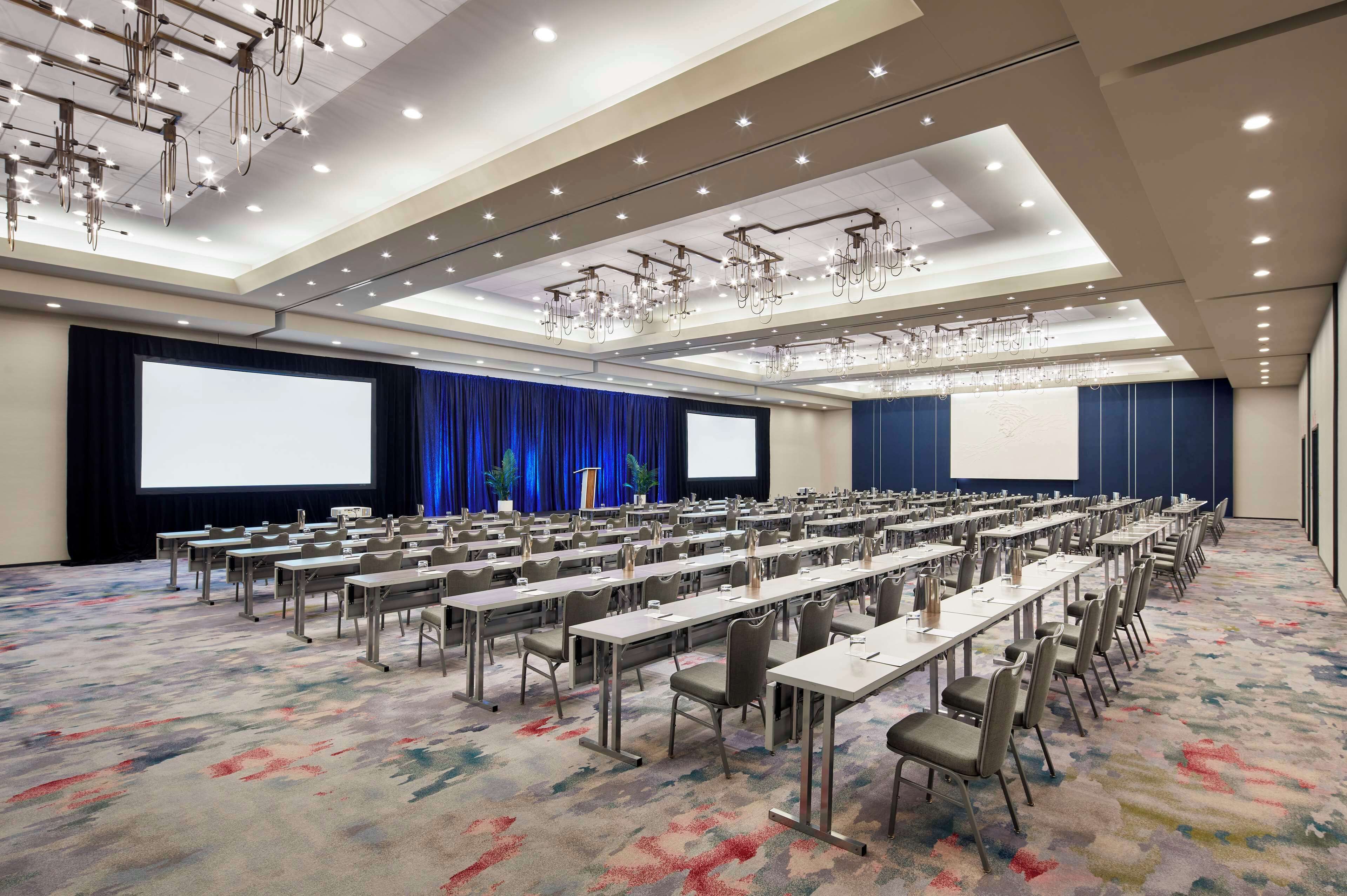 A conference room with rows of tables and chairs, a large screen, and a projector.