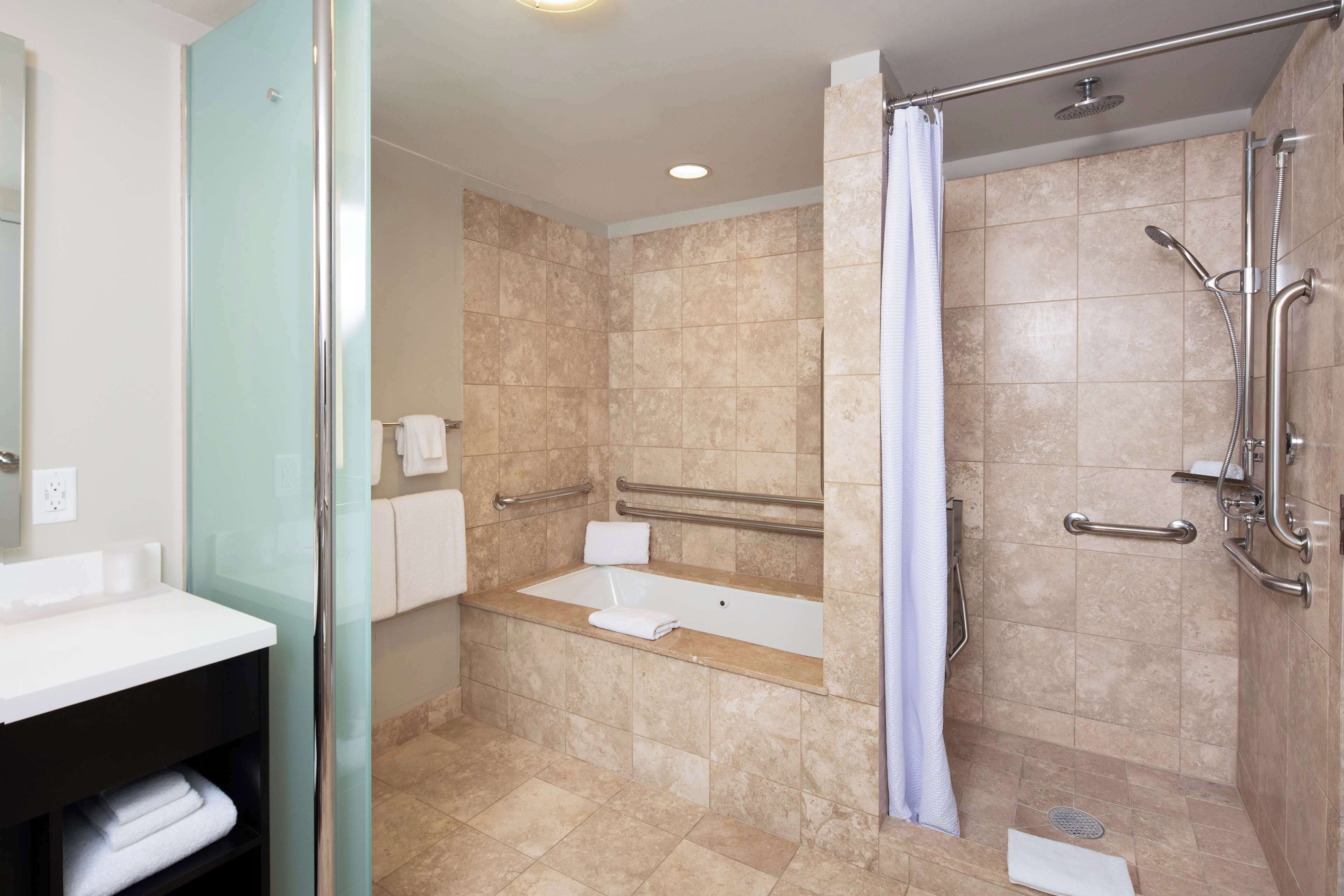 A modern bathroom with a glass-enclosed shower, a bathtub, and a vanity with a sink and towel rack.