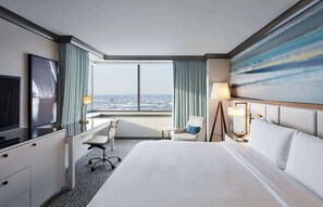 A hotel room with a bed, desk, chair, TV, and a large window with a city view. - The Lofton Hotel, Tapestry Collection by Hilton (Minneapolis)