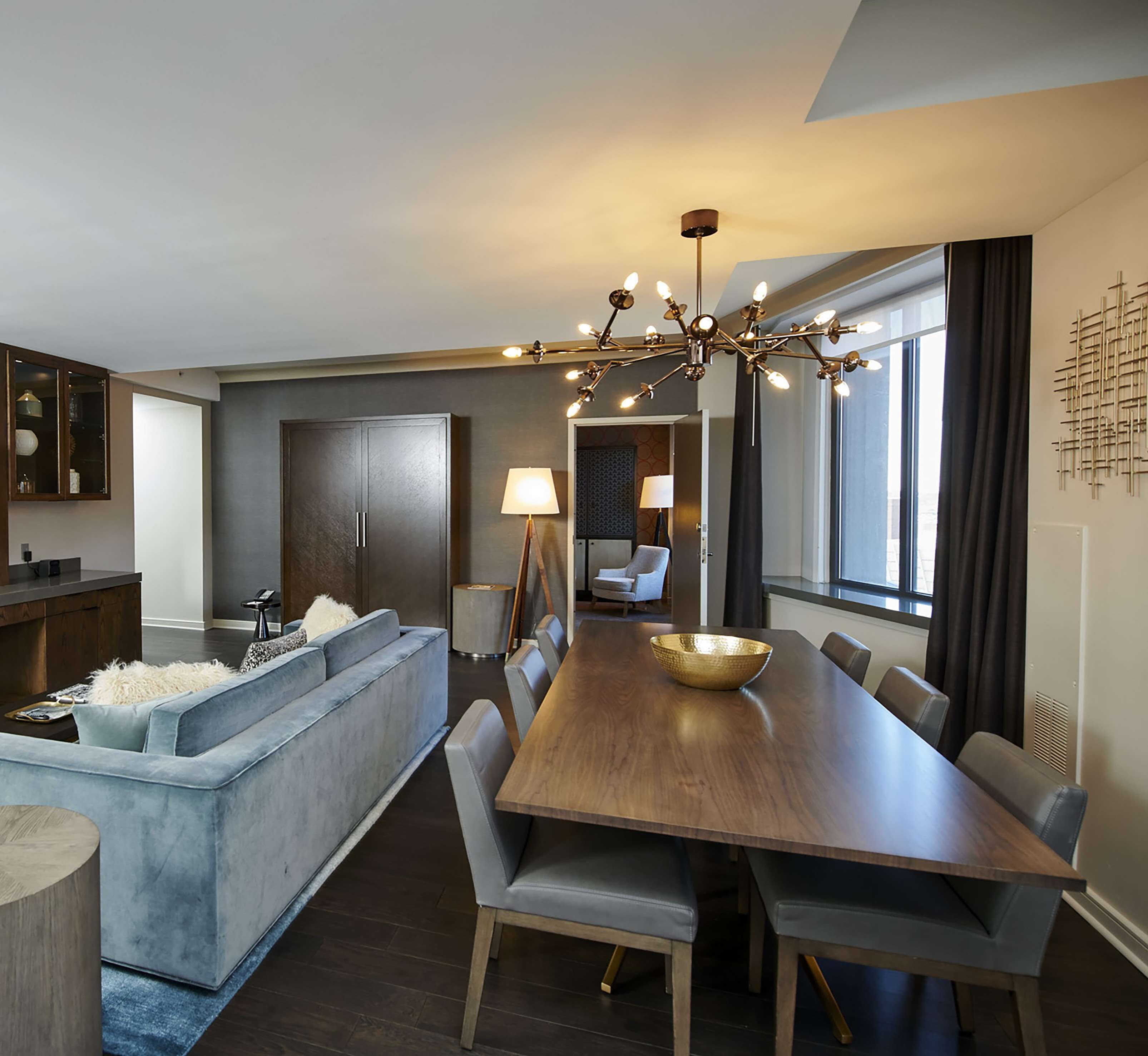 A modern dining area with a wooden table and chairs, a sofa, and a chandelier.