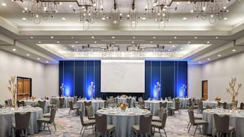 Un salón de conferencias amplio con mesas redondas, sillas y una pantalla grande.