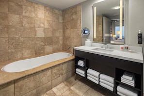 A modern bathroom with a bathtub, a large mirror, and a vanity with towels.