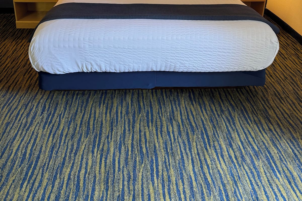 Habitación de hotel con una cama grande, dos lámparas de noche, una mesita de noche con un teléfono y dos cuadros en la pared.