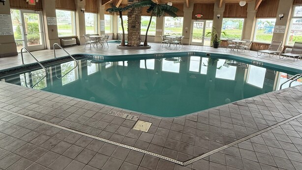 Una piscina interior con un pilar de piedra, techo de madera y suelo de baldosas.