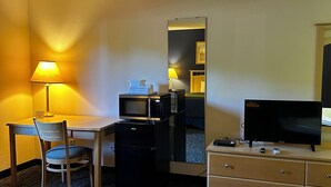 Habitación de hotel con escritorio, silla, microondas, refrigerador, cómoda y televisor.