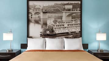 A hotel room with a large bed, two bedside tables with lamps, and a framed picture of a bridge and riverboat on the wall.