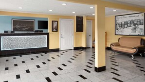 A reception area with a check-in counter, a framed welcome sign, a sofa, and a patterned floor. - Super 8 by Wyndham Whites Creek/ Nashville NW Area (Whites Creek)