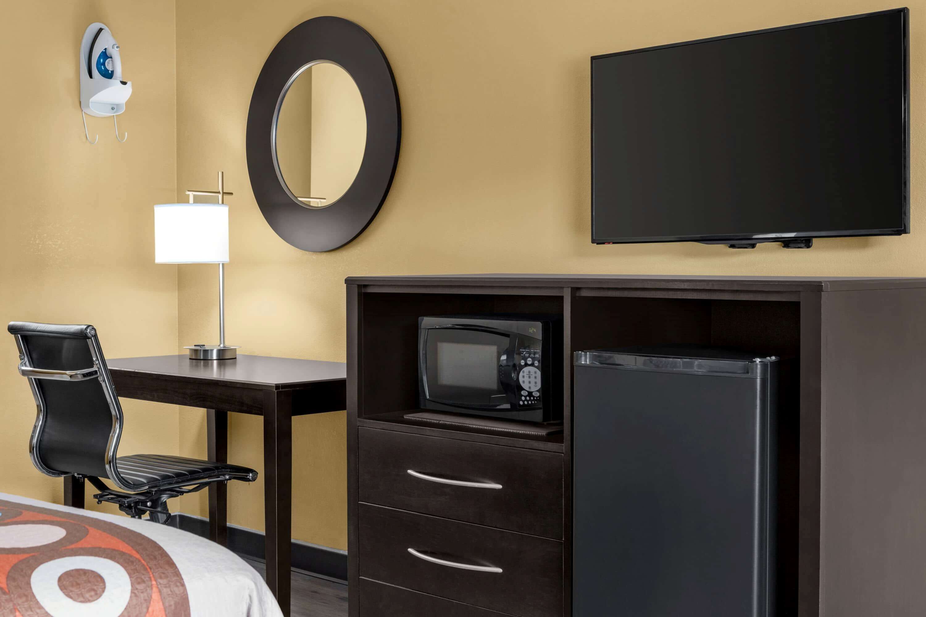 Une chambre d’hôtel équipée d’un lit, d’un bureau avec une chaise, d’un four à micro-ondes, d’un réfrigérateur, d’une télévision, d’un miroir et d’un fer à repasser fixé au mur.