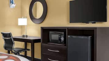 Une chambre d’hôtel équipée d’un lit, d’un bureau avec une chaise, d’un four à micro-ondes, d’un réfrigérateur, d’une télévision, d’un miroir et d’un fer à repasser fixé au mur.