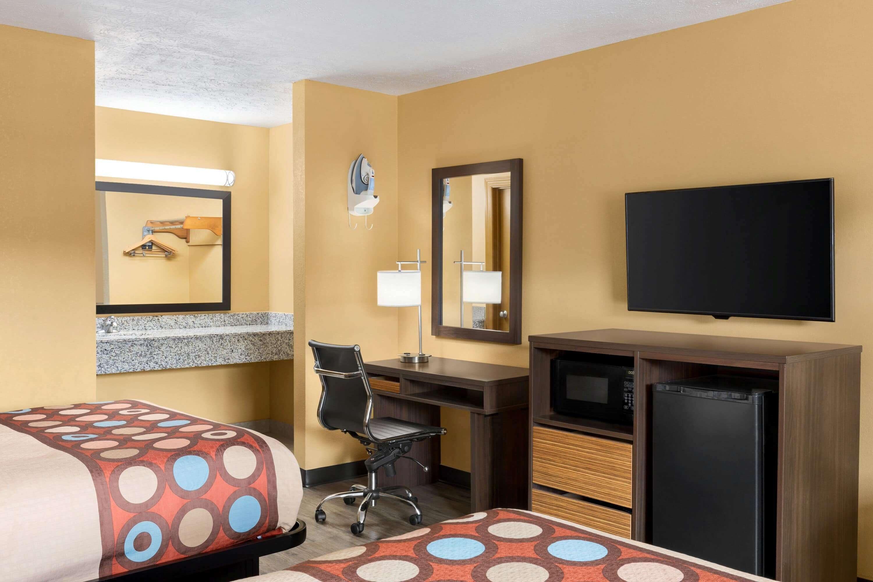 A hotel room with two beds, a desk, a chair, a television, and a refrigerator.