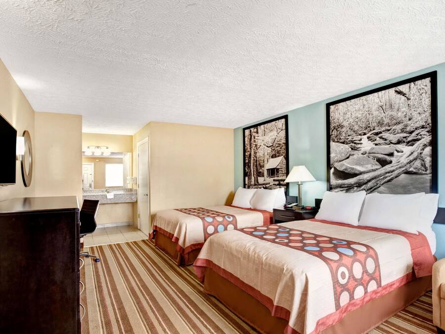 Una camera d'albergo con due letti, una scrivania, una sedia, una TV e un bagno sullo sfondo.