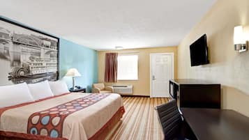 A hotel room with a large bed, a flat-screen TV, a desk, a chair, a window with curtains, and a wall-mounted TV.