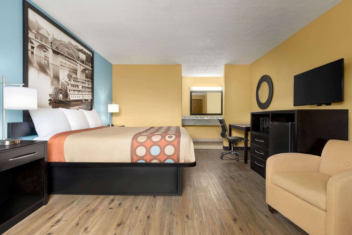 A hotel room with a bed, a desk, a chair, a TV, and a large mirror.