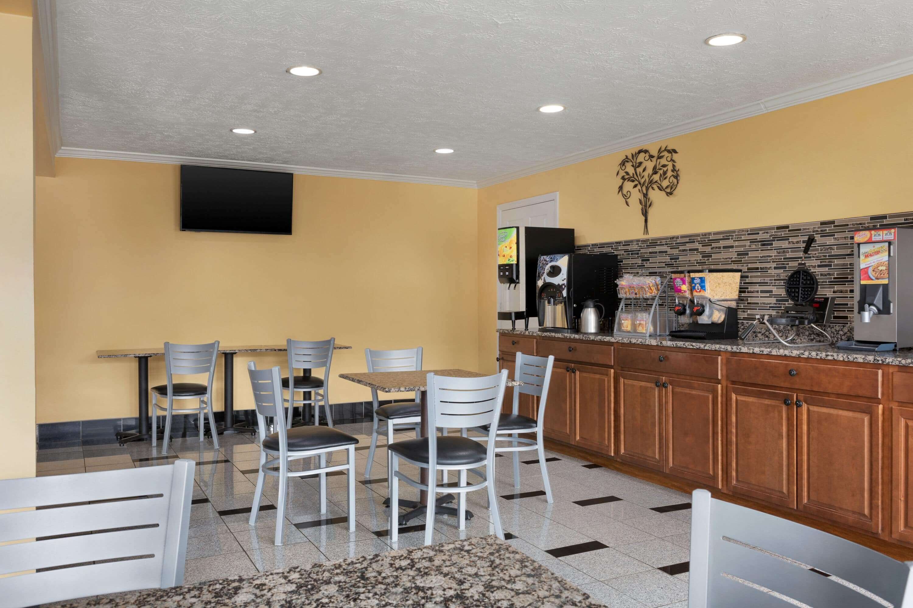 A modern kitchen with granite countertops, wooden cabinets, and a flat-screen TV mounted on the wall.