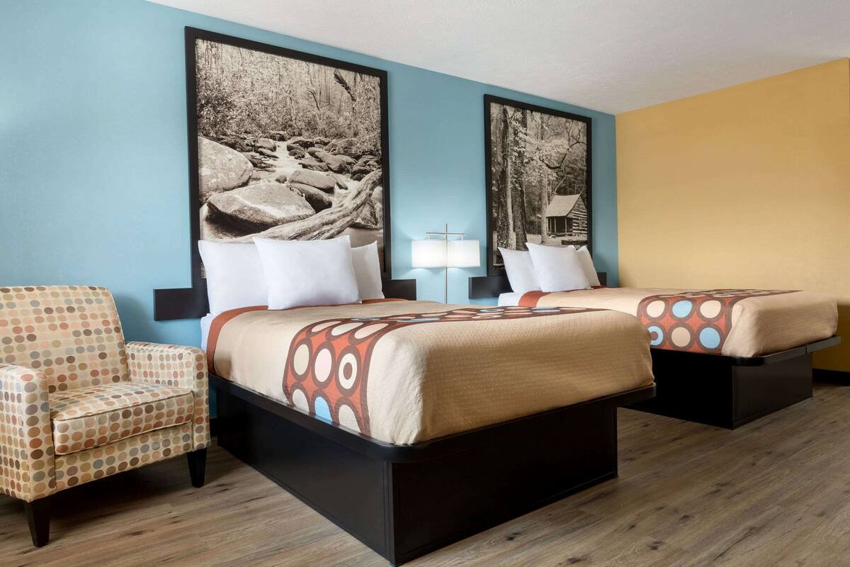 A hotel room with two beds, a polka dot armchair, and large framed pictures on the walls.
