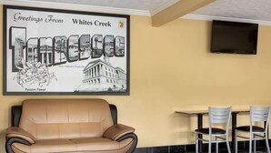 A lobby with a tan leather sofa, two white chairs, a small table, and a wall-mounted TV. A large framed poster of Whites Creek, Tennessee, is visible. - Super 8 by Wyndham Whites Creek/ Nashville NW Area (Whites Creek)