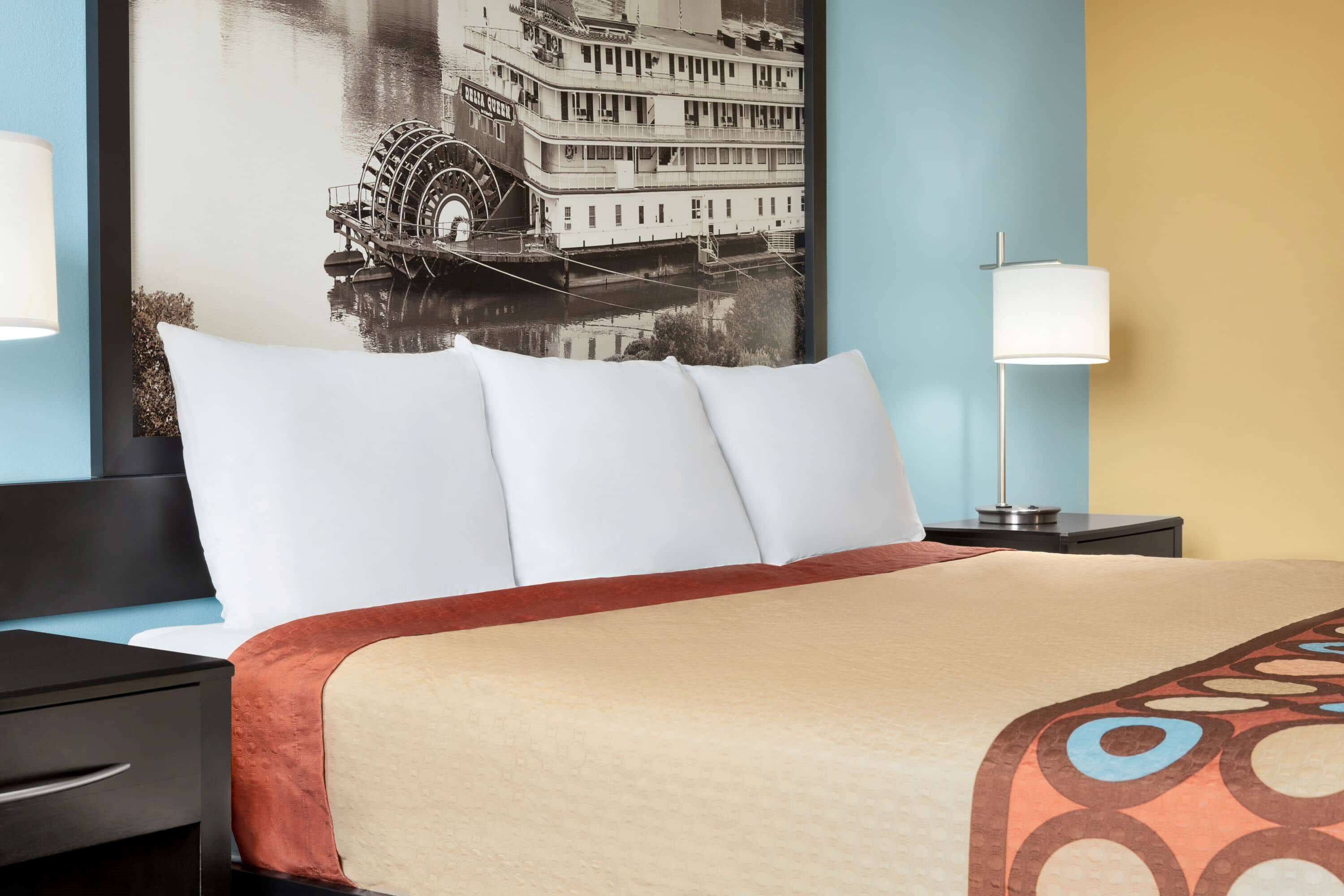 A hotel room with a large bed, a nightstand with a lamp, and a wall-mounted picture of a historic building.
