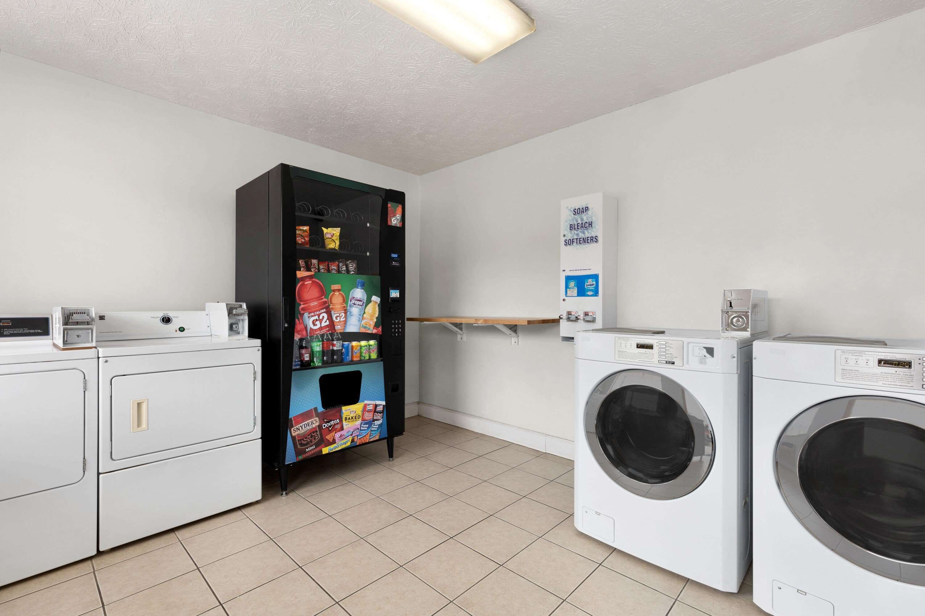 A laundry room with a vending machine, two washing machines, and a shelf with soap and detergent.