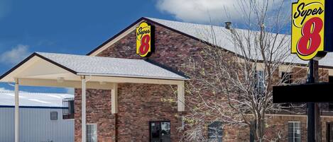 Un motel de type Super 8 avec une façade en briques, un espace de stationnement couvert et un ciel d’un bleu limpide.