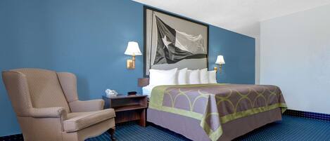 A hotel room with a bed, a chair, a nightstand, and a wall-mounted flag.
