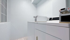 A laundry area with a washing machine and dryer, a window with blinds, and a tiled floor.
