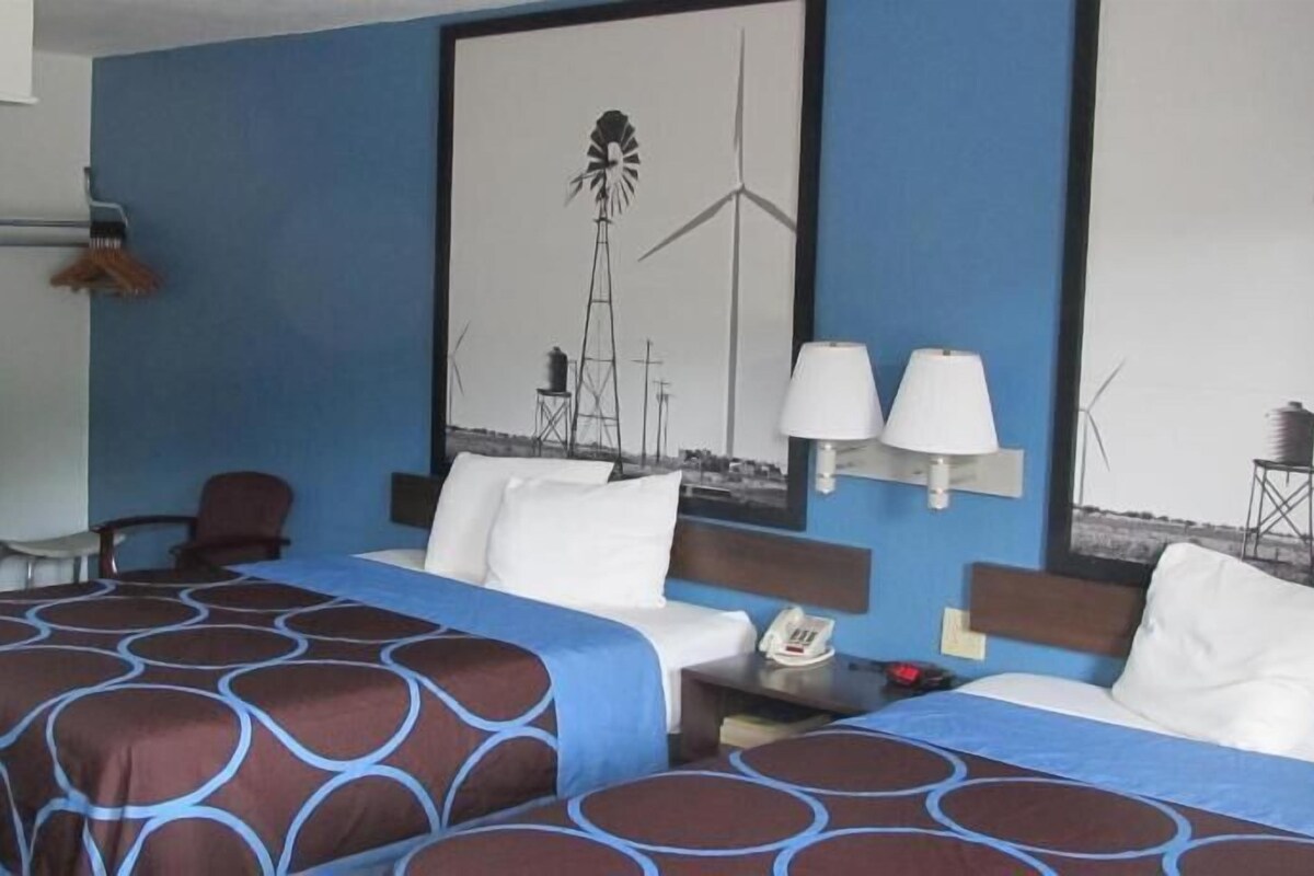Habitación de hotel con cama, escritorio con teléfono, silla, microondas y lámpara de pared.