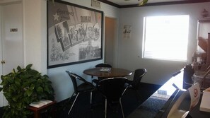 Quarto privativo com uma mesa redonda, quatro cadeiras, um vaso de planta, um quadro com uma imagem do Texas e uma janela com persianas.