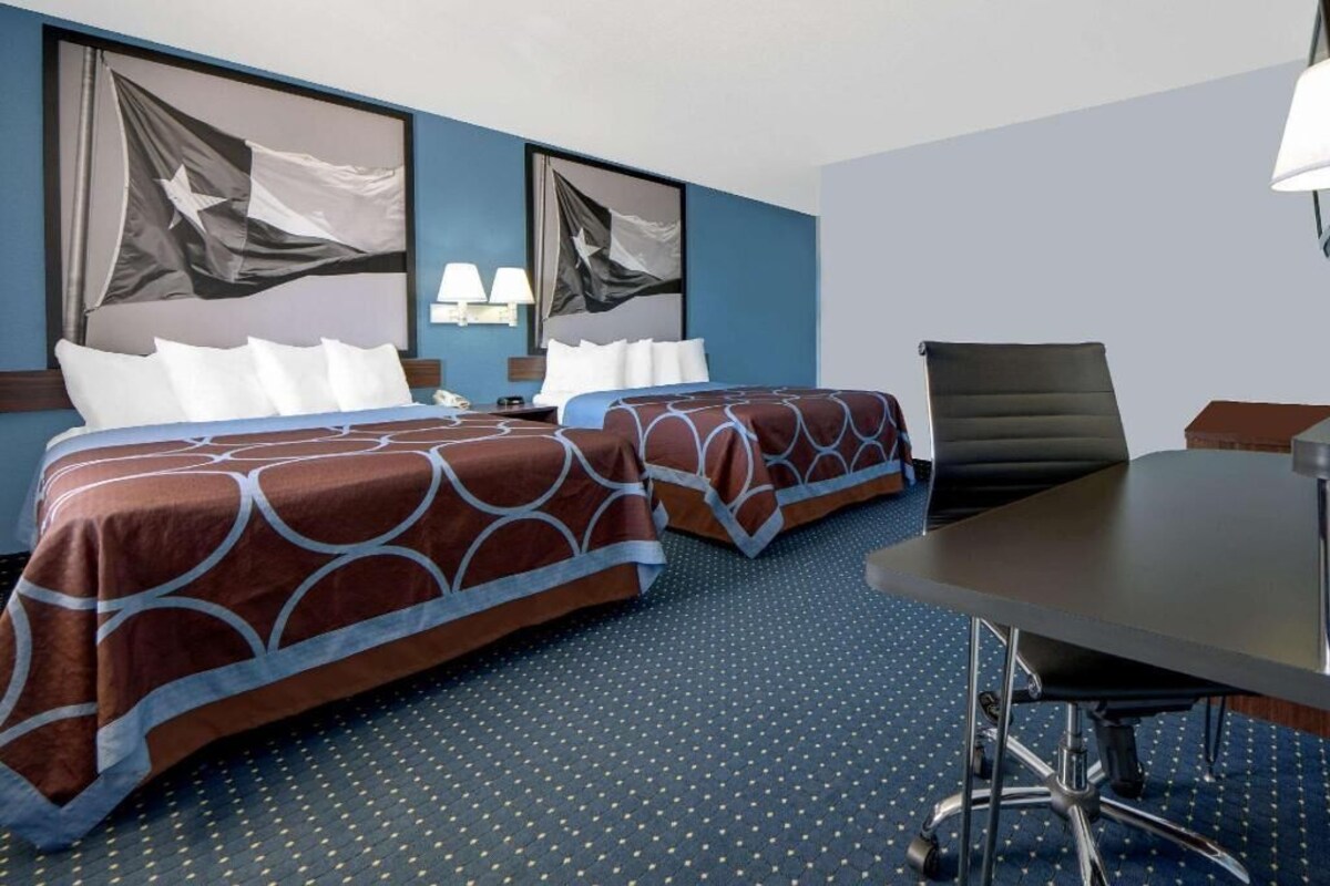 Habitación de hotel con dos camas, un escritorio, una silla y dos lámparas de pared.