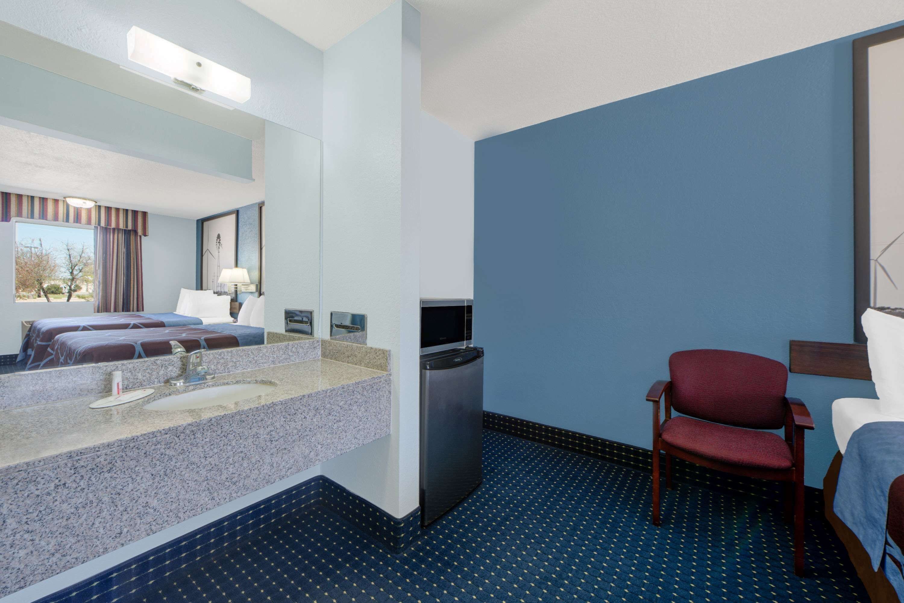 A hotel room with a bed, a desk, a chair, a sink, and a mirror.