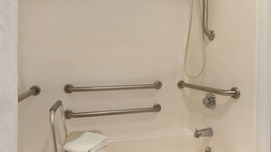Ein Badezimmer mit Badewanne, Haltegriffen, Duschkopf und Handtuch.