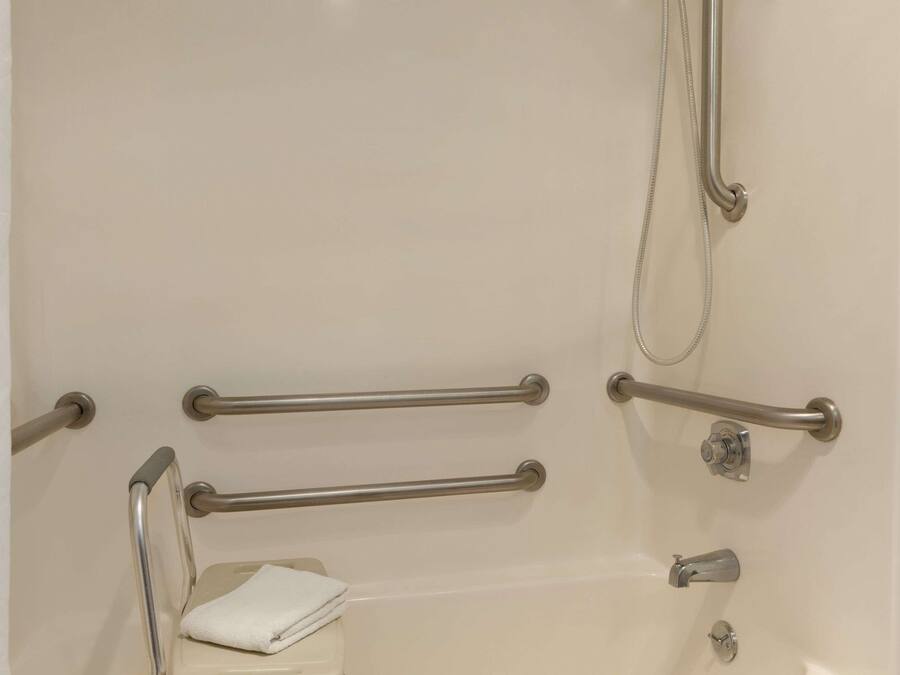 Une salle de bain équipée d’une baignoire, de barres d’appui, d’un pommeau de douche et d’une serviette.