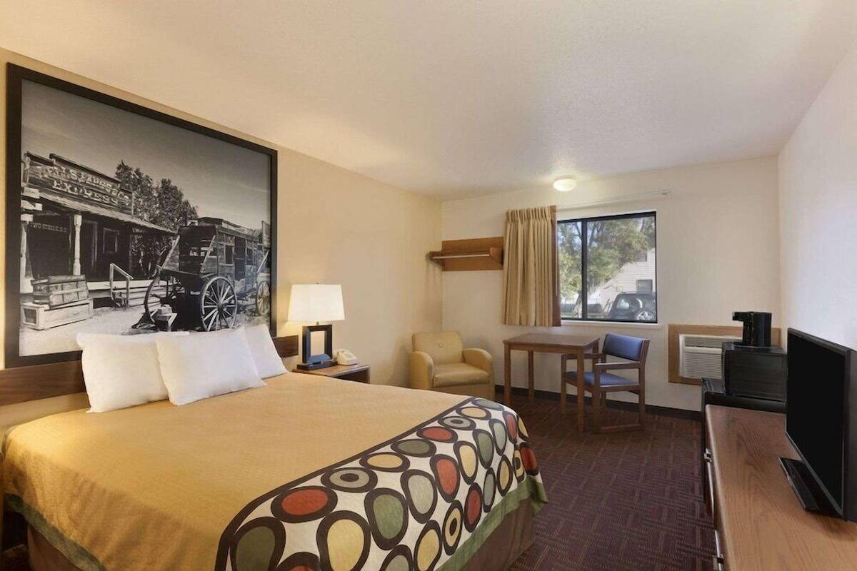 A hotel room with a bed, a desk, a chair, a television, and a window with curtains.