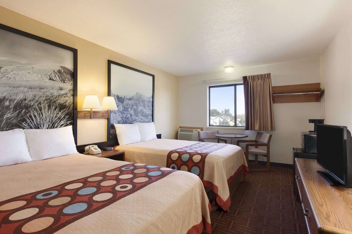 A hotel room with two beds, a desk, a chair, a television, and a window with curtains.