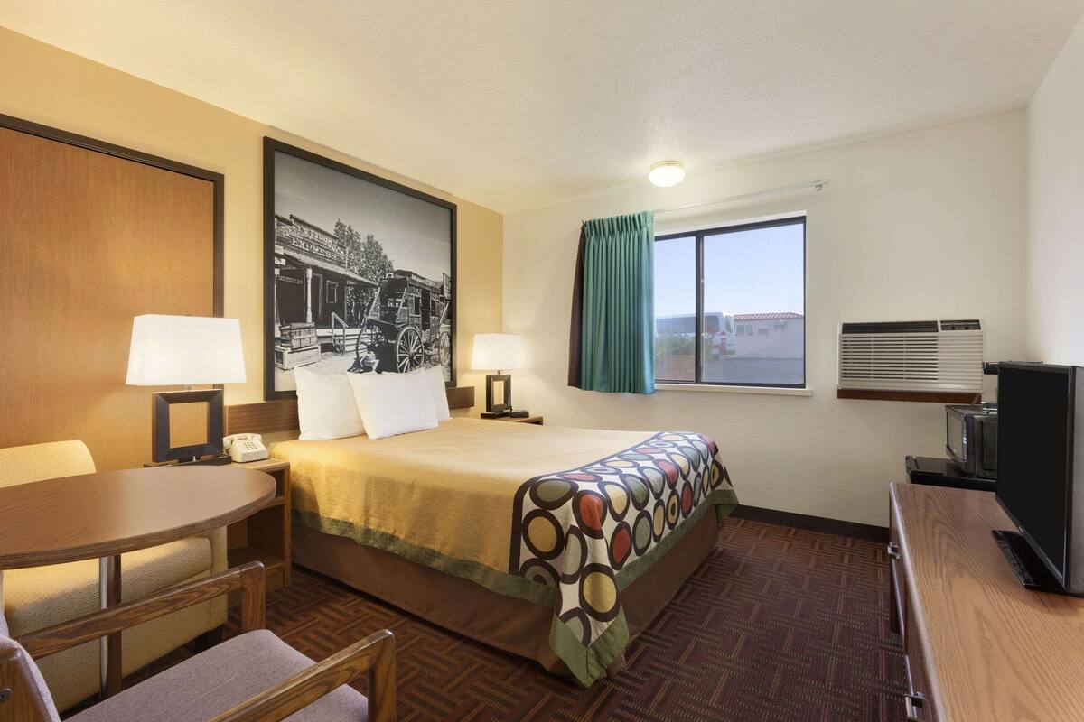 A hotel room with a bed, a desk, a chair, a television, and a window with curtains.