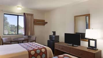 Una habitación de hotel con una cama, un escritorio, un televisor, una lámpara y un ventanal con cortinas.