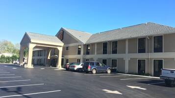A hotel with a covered entrance, multiple parking spaces, and a clear blue sky.