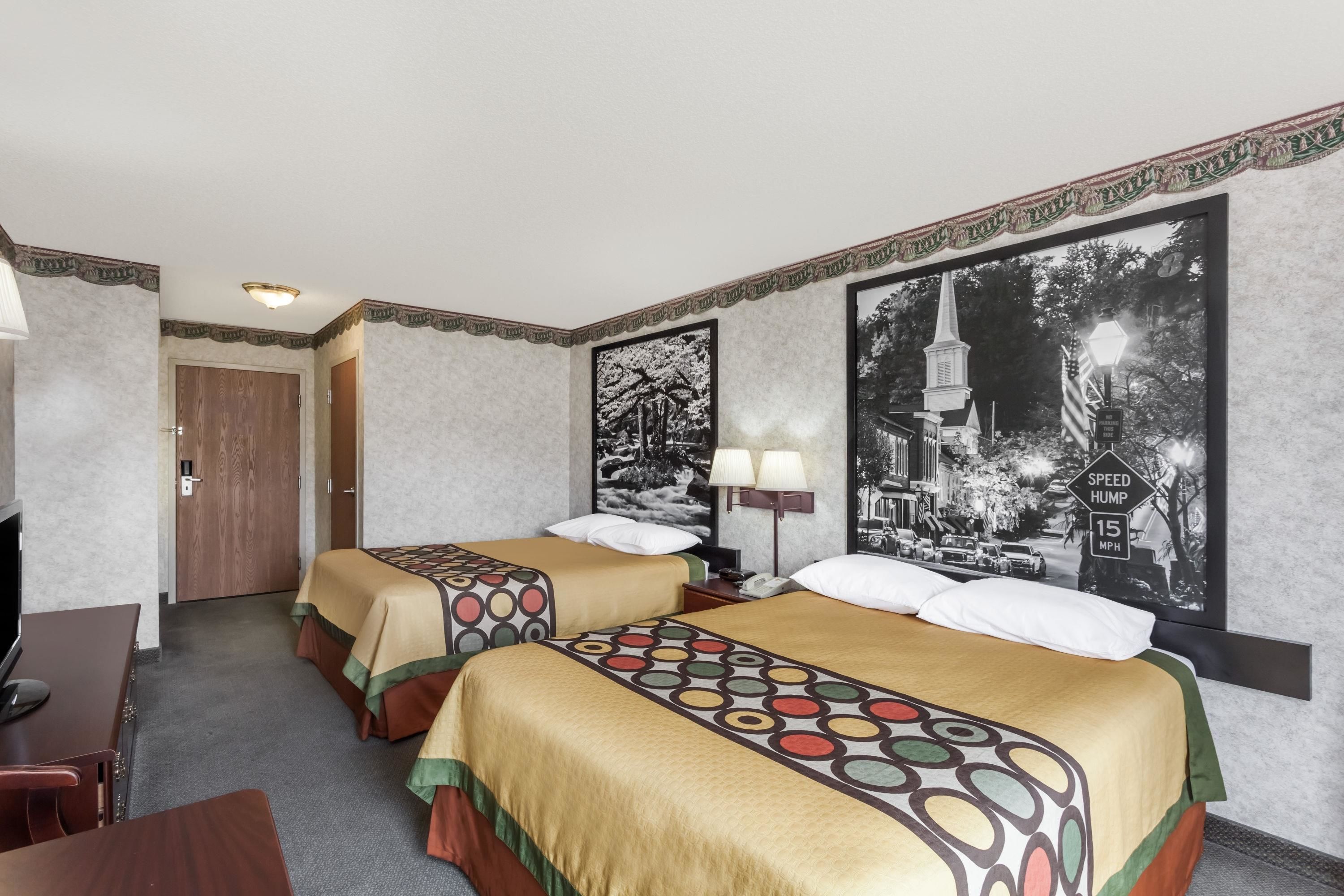 Hotellihuone, jossa on kaksi sänkyä, työpöytä, tuoli ja suuri kehystetty taulu seinällä.