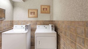 Une buanderie équipée de deux lave-linge et deux sèche-linge Whirlpool, avec un dosseret carrelé et des tableaux encadrés accrochés au mur.