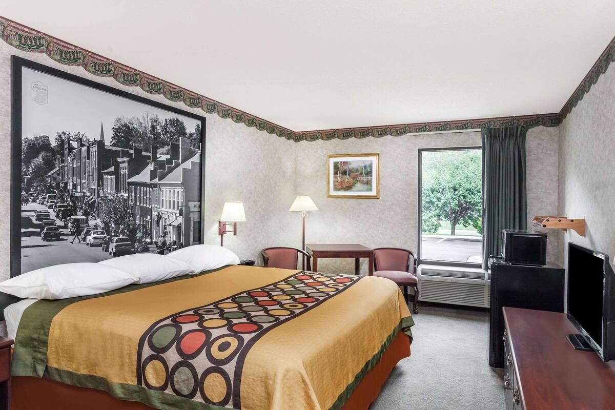 Une chambre d’hôtel avec un grand lit, un bureau, une chaise, une télévision et une fenêtre avec des rideaux.